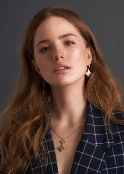 a woman with long red hair wearing a blue jacket and gold earrings is looking at the camera