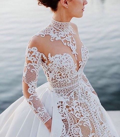 a woman wearing a white wedding dress with sheer lace on the sleeves and neckline