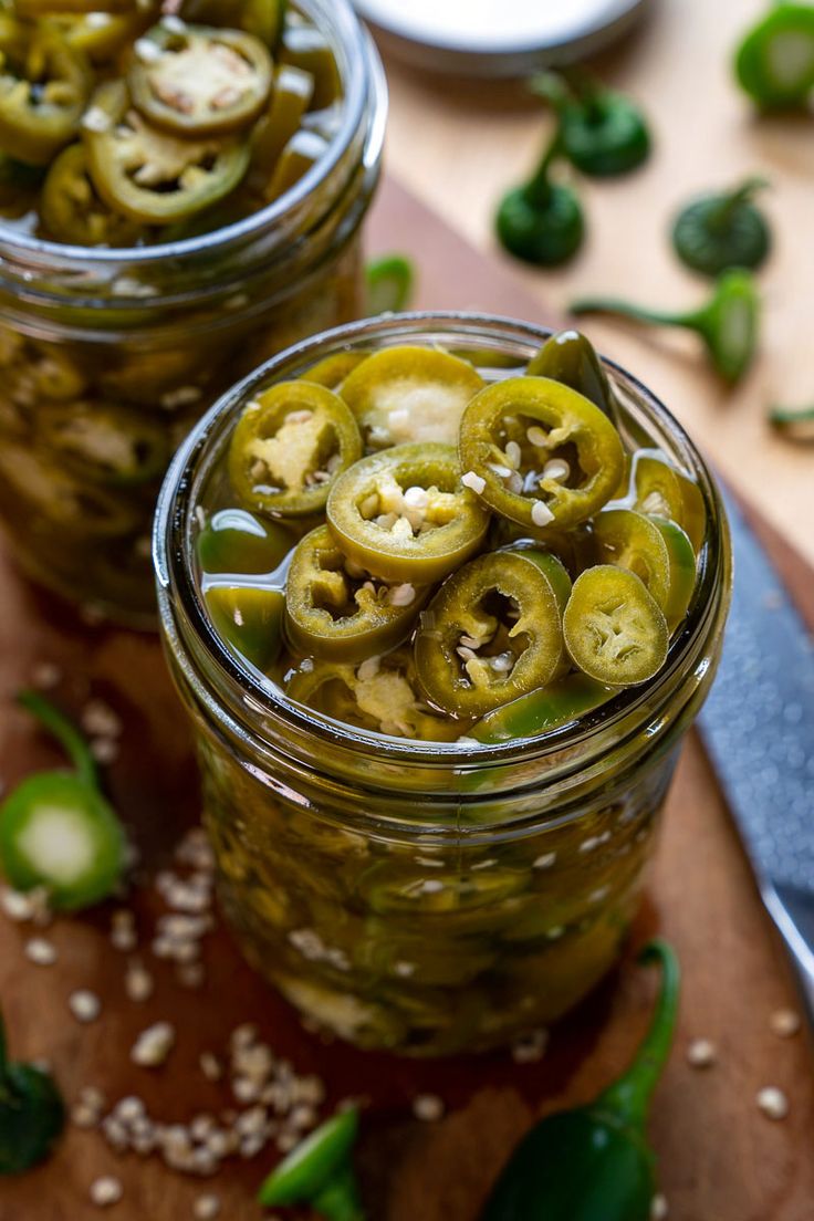 two jars filled with pickles on top of a cutting board