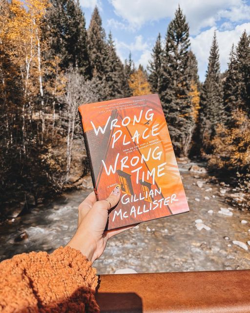 a person holding up a book in front of a river and trees with the words wrong place wrong time written on it