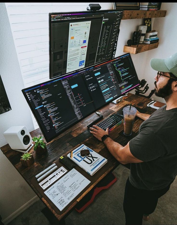 a man sitting at a desk in front of two computer monitors and a laptop on it