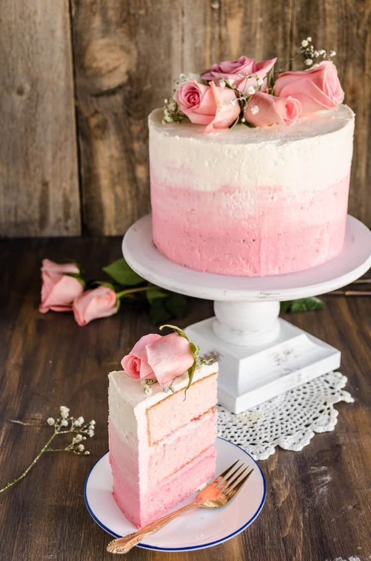 a pink cake with white frosting and flowers on top is sitting on a plate