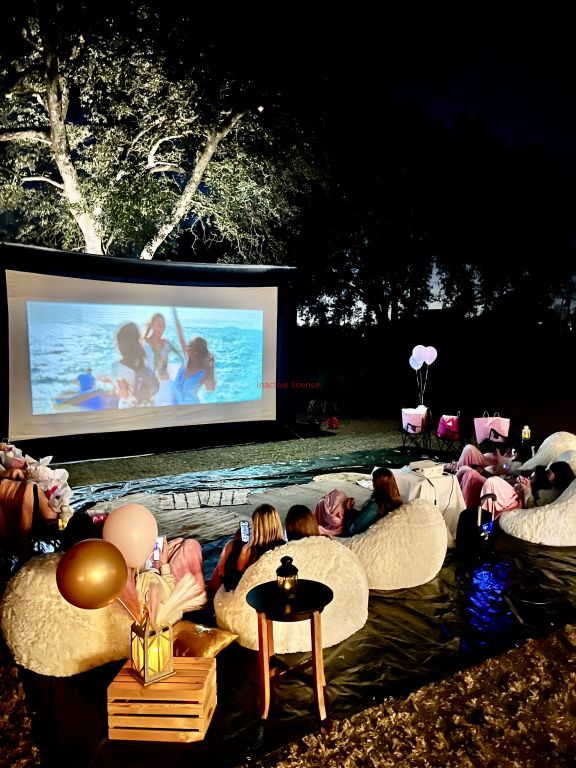 an outdoor movie theater with people sitting on bean bags in the water at night time