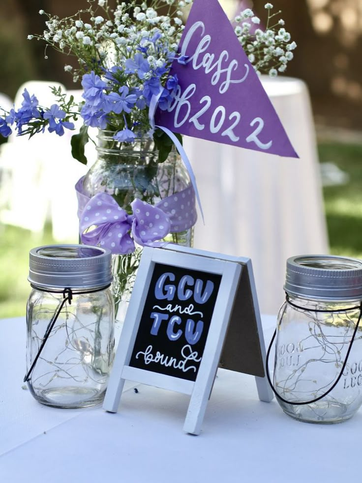 mason jars filled with blue flowers are sitting on a table next to a chalkboard sign