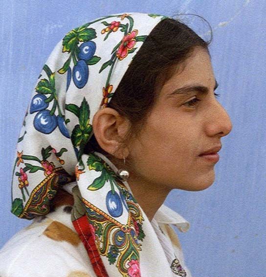 a woman with a scarf on her head looking off into the distance while standing in front of a blue wall