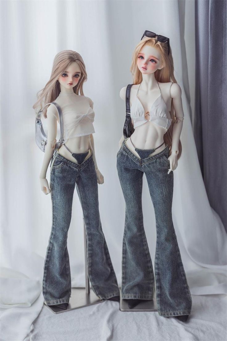 two dolls standing next to each other in front of a white curtain