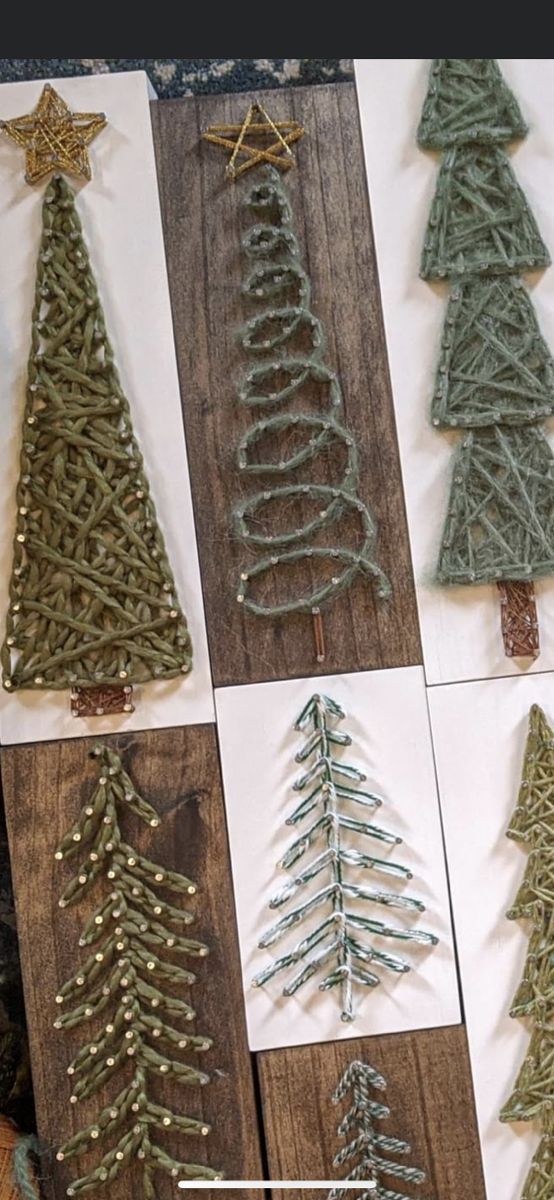 christmas trees made out of yarn are displayed on a wooden board with string and star decorations