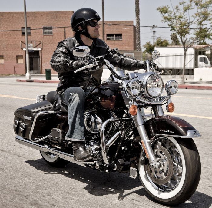 a man riding on the back of a black motorcycle down a street next to a brick building