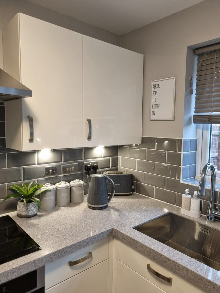 a kitchen with white cabinets and gray tile backsplash, stainless steel sink and stove