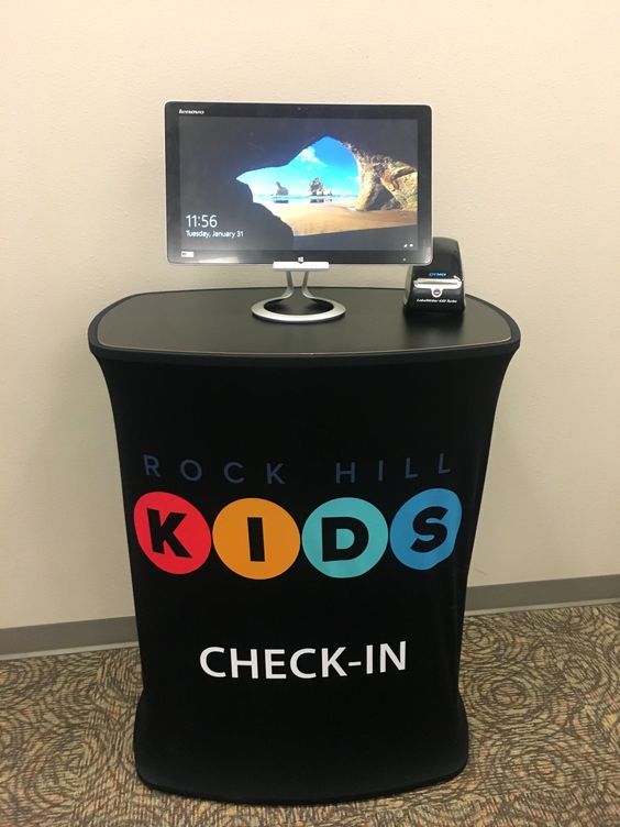 a computer monitor sitting on top of a black stand with kids check - in written on it