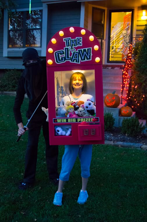 a woman standing next to a man in front of a house with a fake claw machine