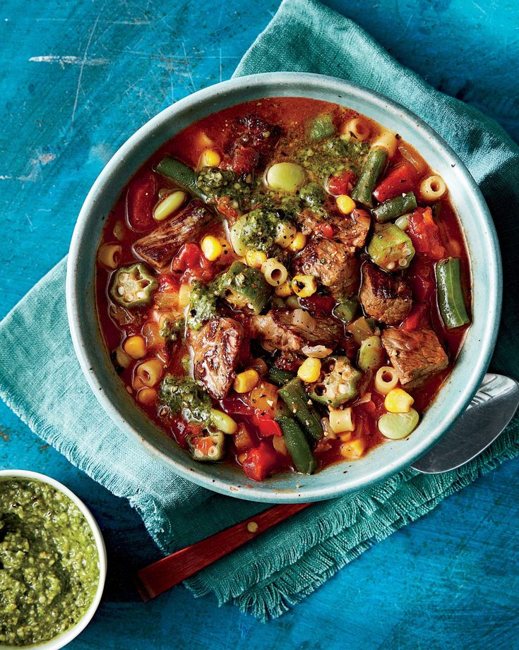 a bowl filled with meat and vegetables next to a small bowl of pesto sauce