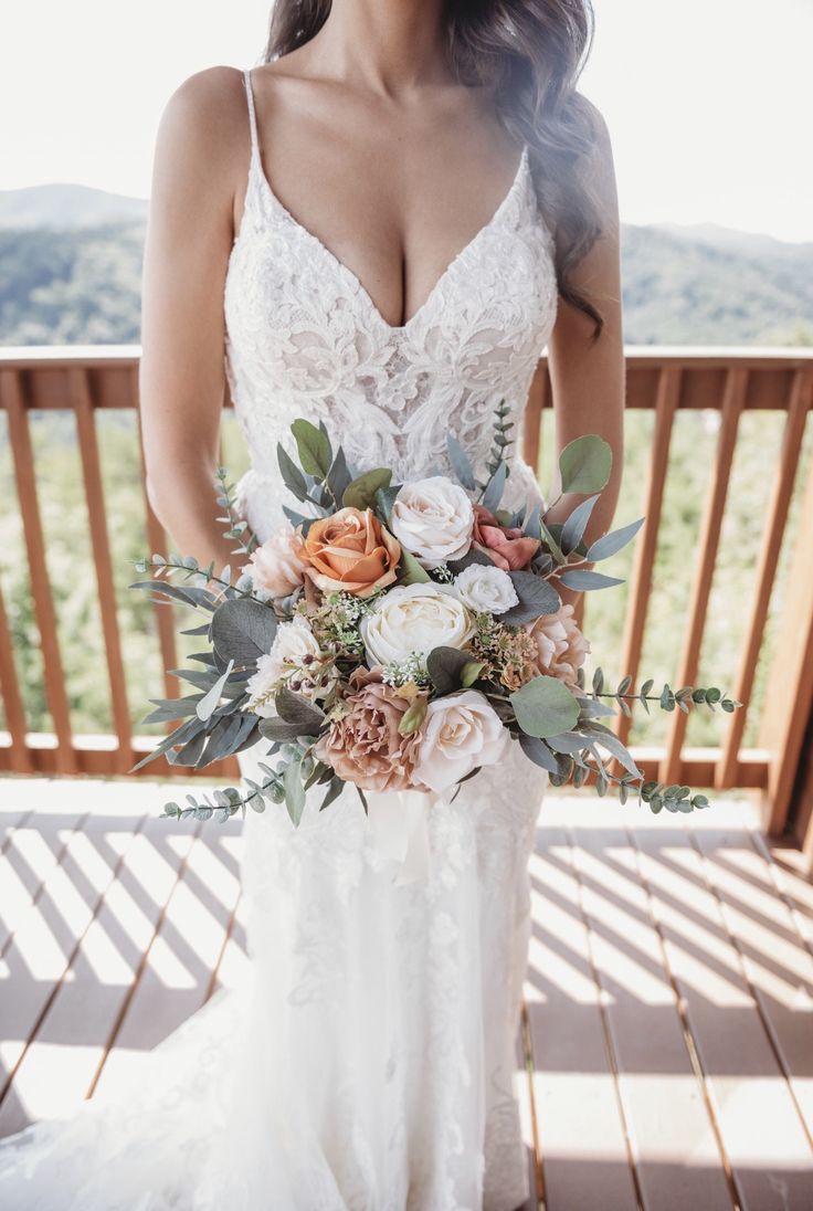 a woman in a wedding dress holding a bridal bouquet on a deck with mountains in the background