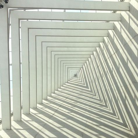 an image of a long white hallway with shadows on the wall and floor in it