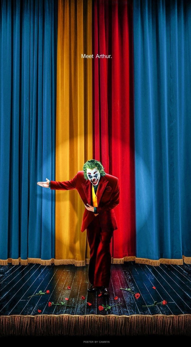 a man dressed as the joker standing in front of a colorful curtain with his arms out