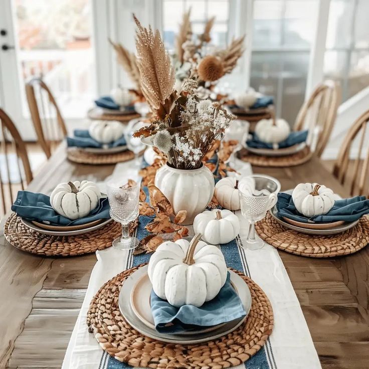 a dining room table set with white pumpkins and blue napkins