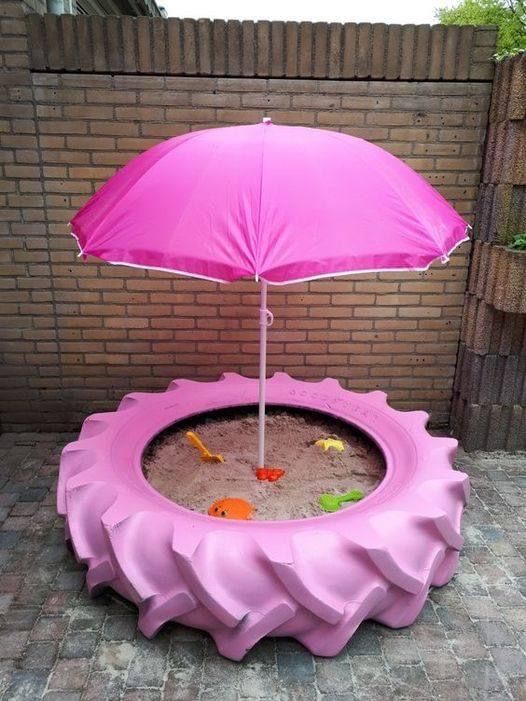 a pink umbrella sitting on top of a sand pit in front of a brick wall