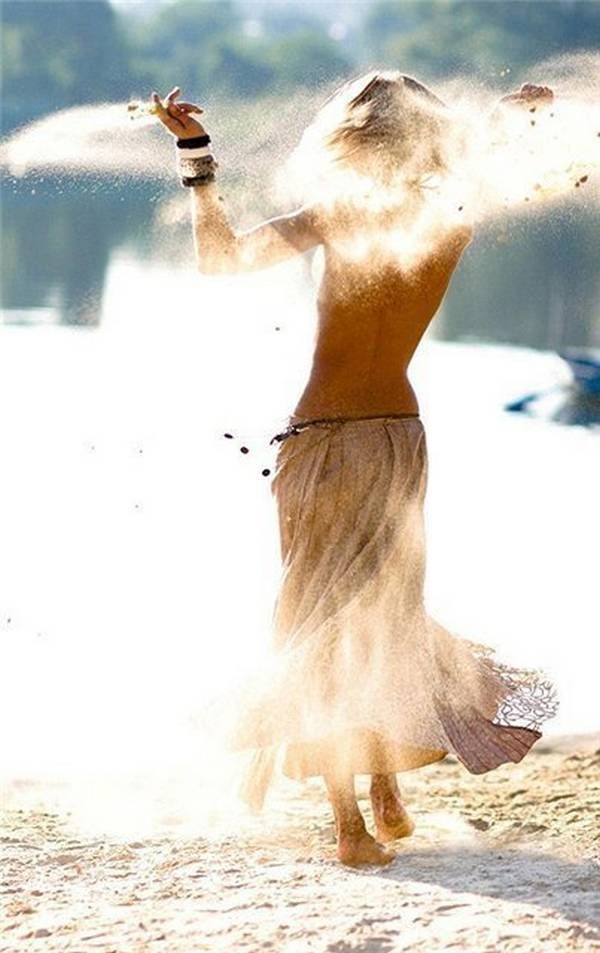 a woman standing on top of a beach next to the ocean with her arms in the air