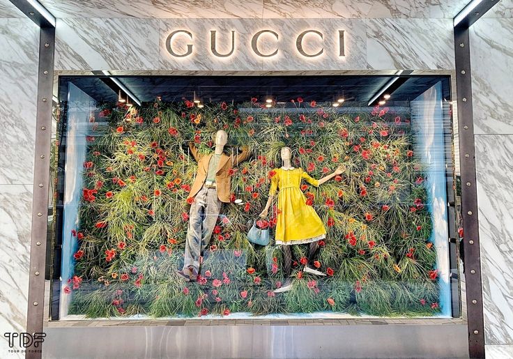 a window display with two mannequins dressed in yellow dresses and red flowers