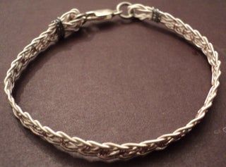 a silver bracelet on a brown surface with the clasp undone to show it's twisted design