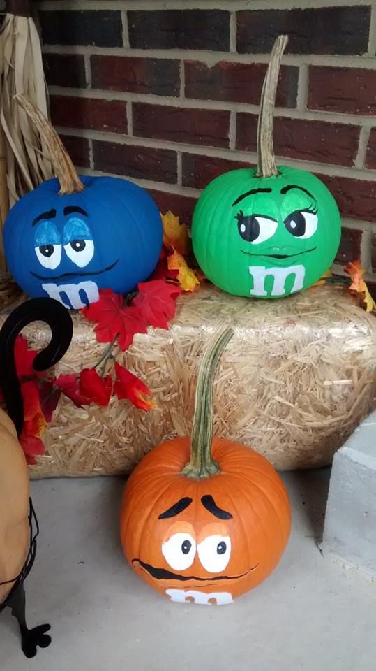 three pumpkins with faces painted on them sitting in front of a brick wall and some hay