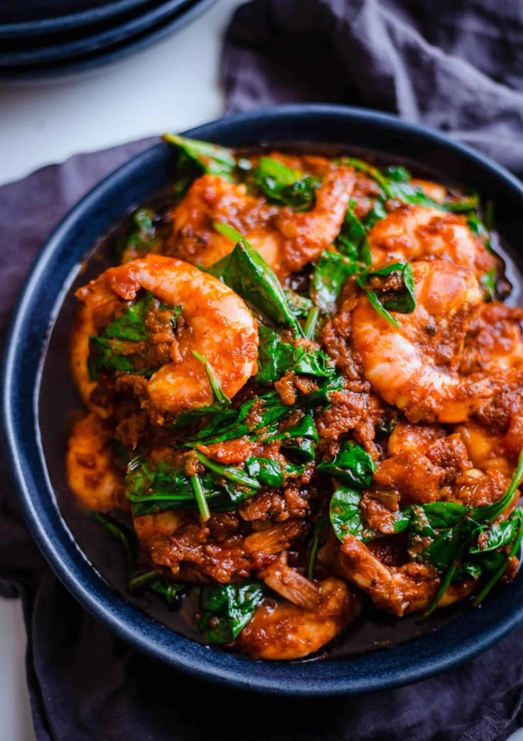 a blue bowl filled with shrimp and spinach