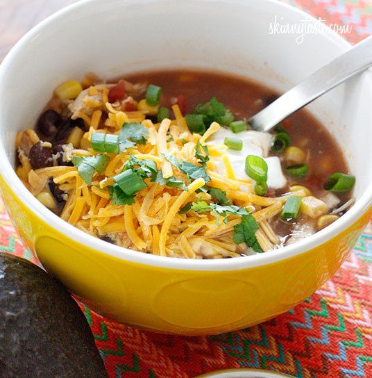 a yellow bowl filled with taco soup next to an avocado and cilantro