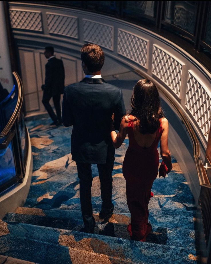 a man and woman walking down an escalator in a building with blue carpet