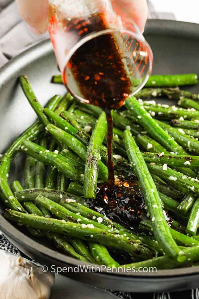 someone pouring sauce on green beans in a skillet