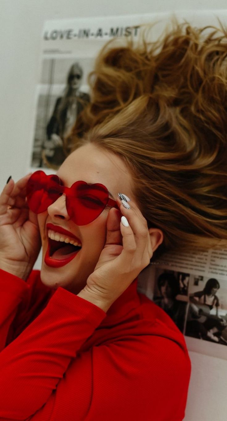 a woman wearing red glasses laying on top of a white wall with her hair blowing in the wind