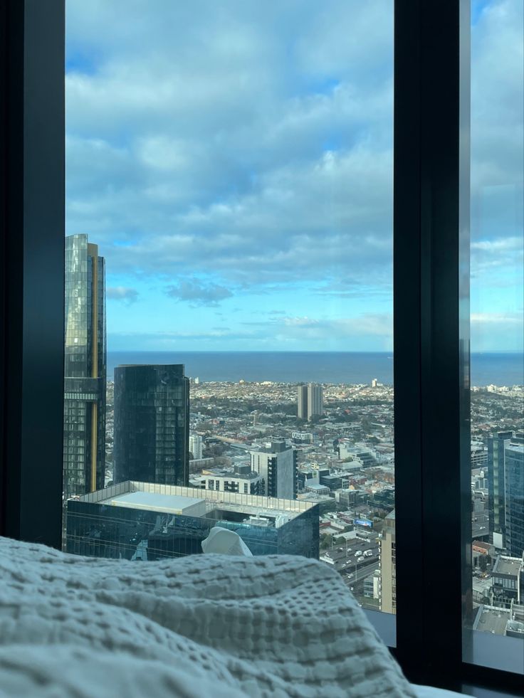 a bed in front of a large window with cityscape and buildings behind it