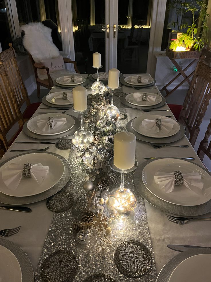 the table is set with silver and white plates, silver napkins, and candles