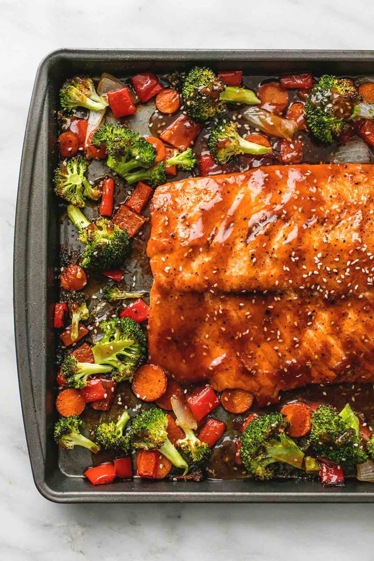 salmon, broccoli and carrots in a baking pan with sesame seeds on top