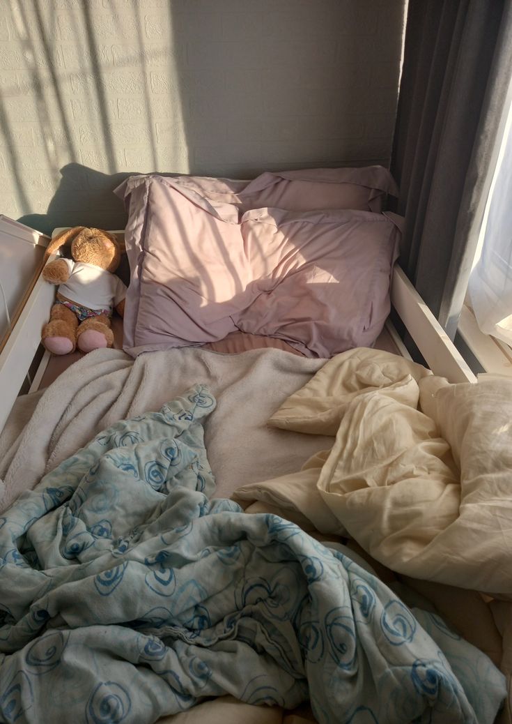 an unmade bed with blankets, pillows and a teddy bear