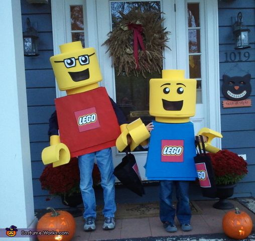 two people dressed as lego characters standing in front of a house