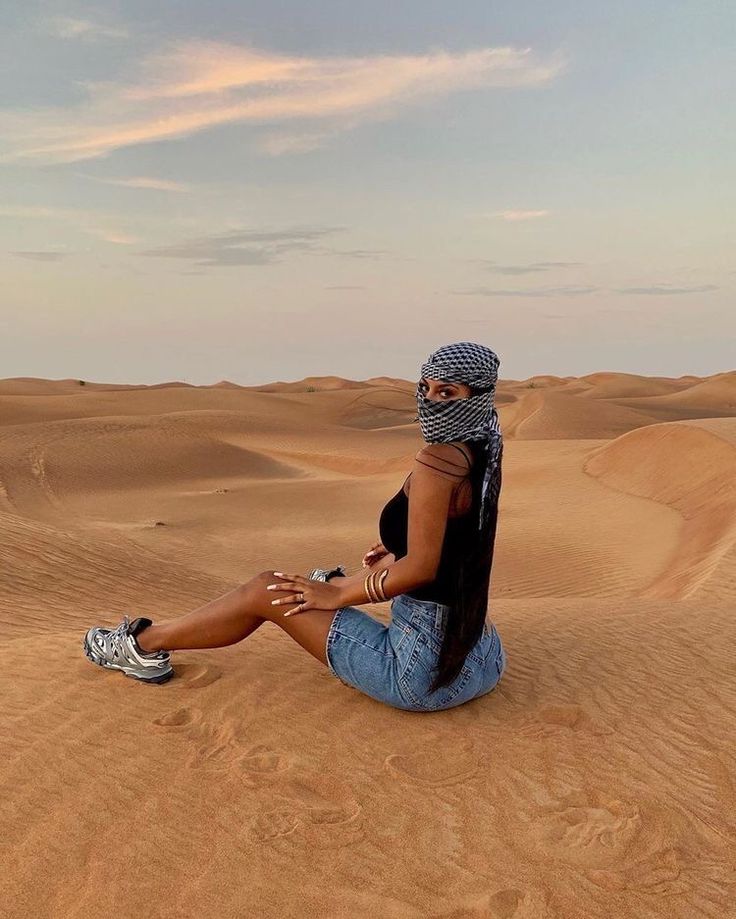 a woman sitting in the middle of a desert with her cell phone to her ear