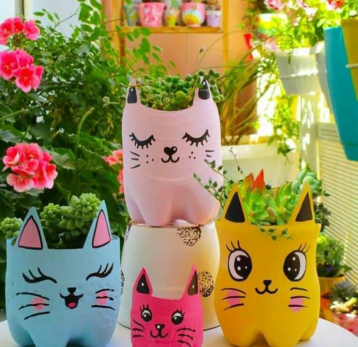 four colorful cat planters sitting on top of a white table next to potted plants