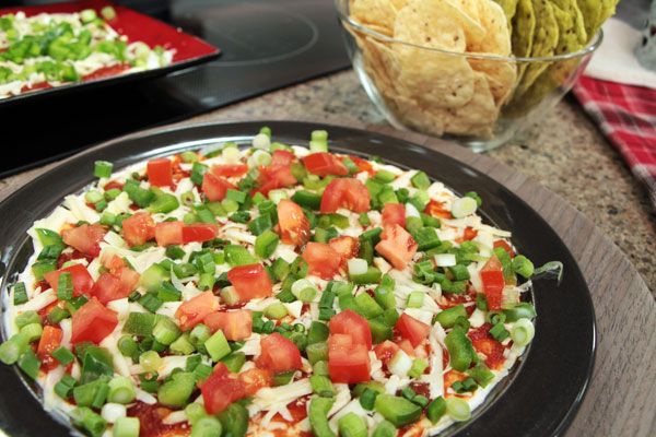 a black plate topped with a pizza covered in veggies next to a bowl of tortilla chips