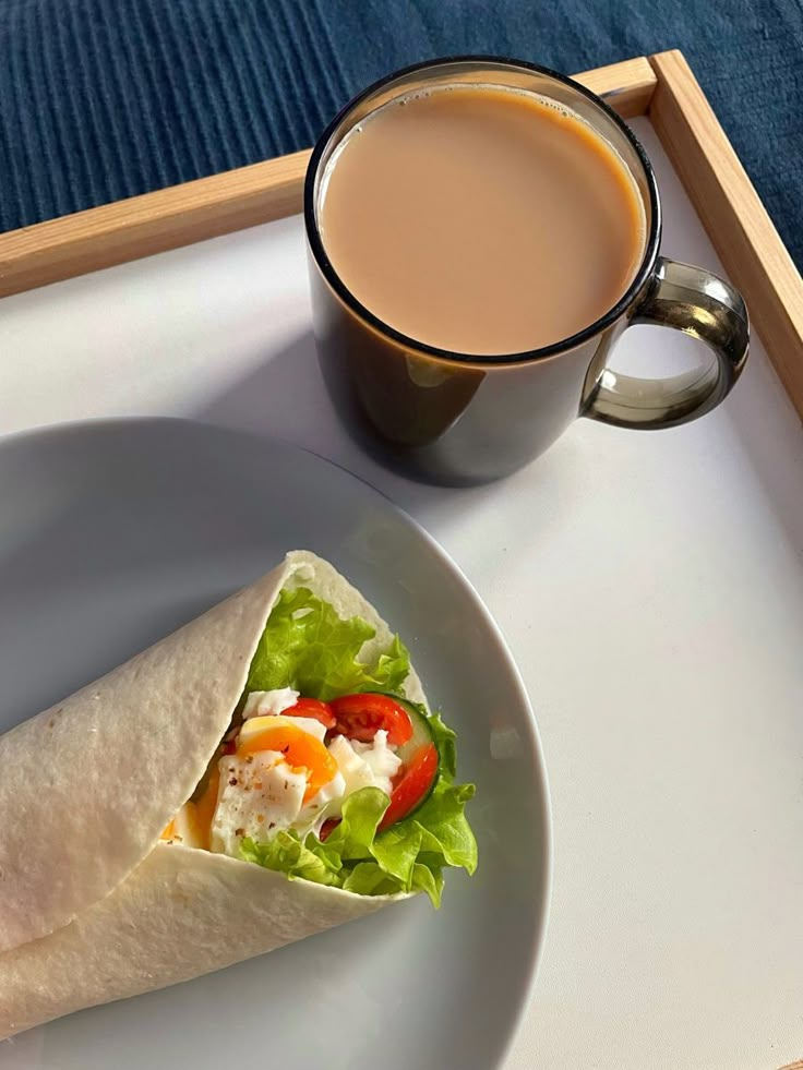 a plate with a burrito next to a cup of coffee and a drink on a tray