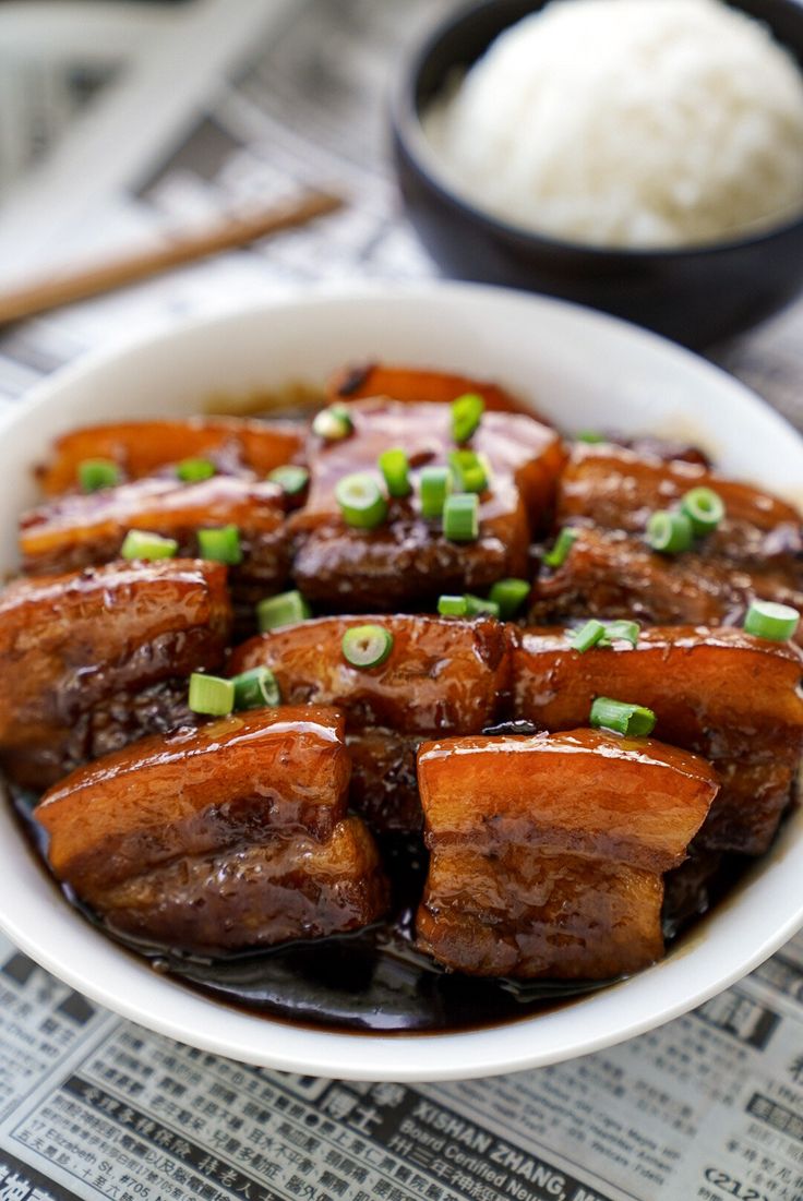 a white bowl filled with meat covered in sauce and green onions on top of a newspaper