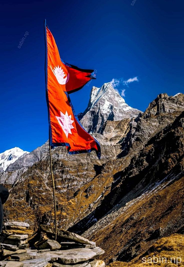 two canadian and canadian flags flying in the wind on top of a rocky mountain range