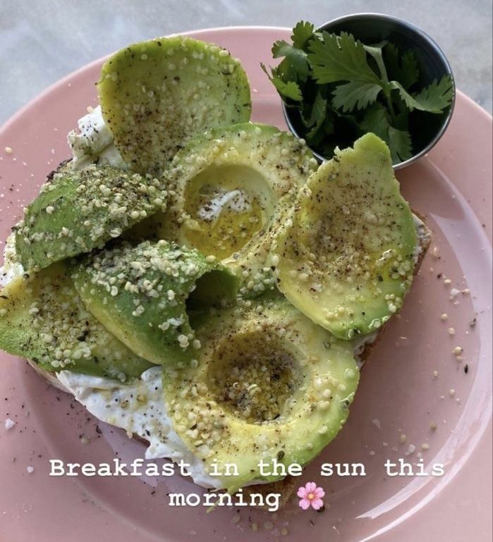 an avocado on a pink plate next to a small bowl of cilantro