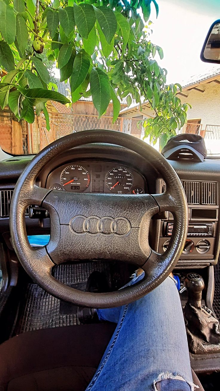 the interior of an old car with blue jeans and leather steering wheel cover on it