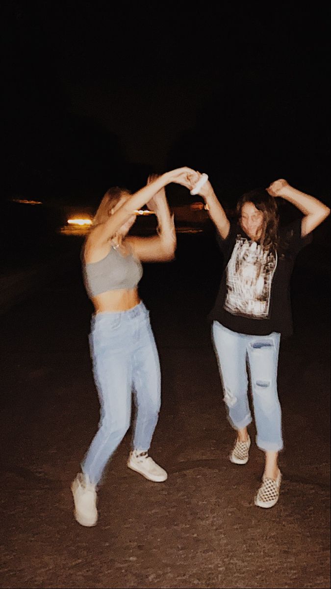 two women are dancing in the street at night with their arms up and hands together