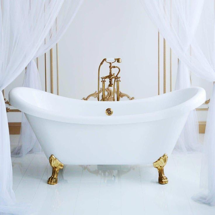 an old fashioned bathtub in a white bathroom with gold fixtures and curtained windows