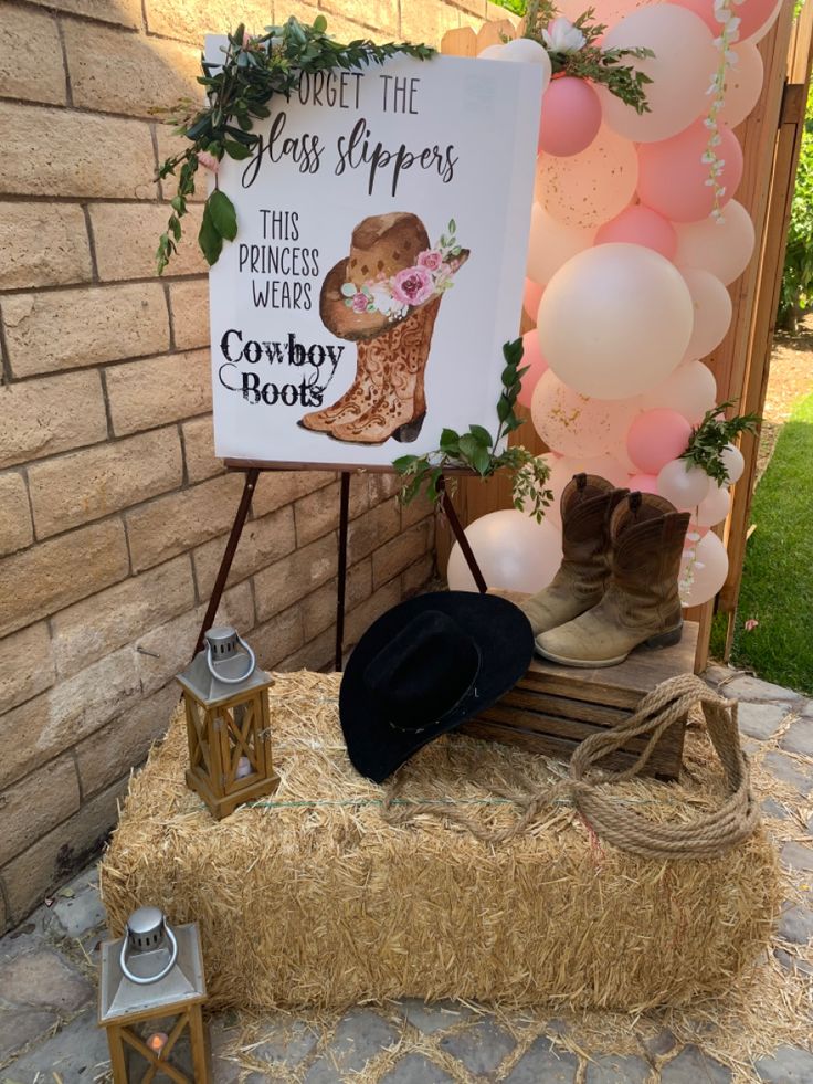 a sign that is on top of hay near some balloons and other items in front of a brick wall