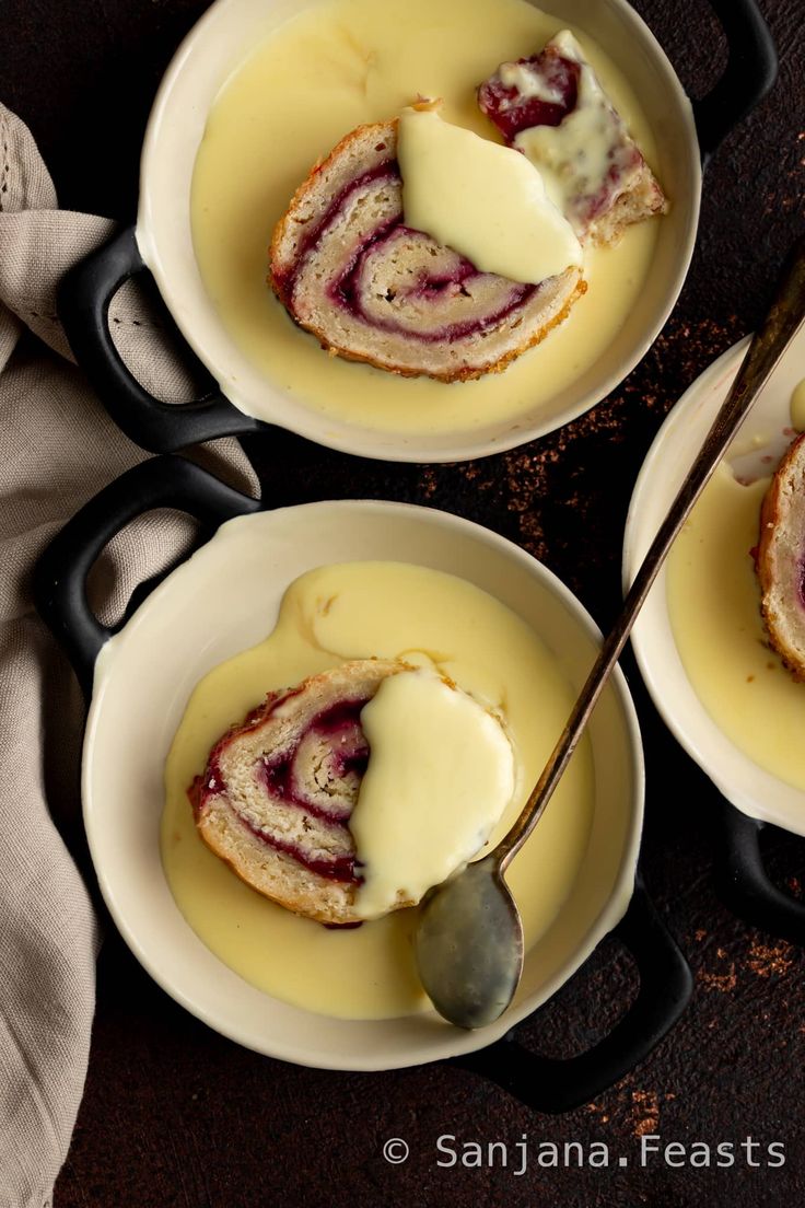 three bowls filled with pudding and cream on top of a wooden table next to two spoons