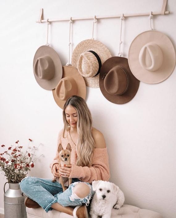 a woman sitting on a bench with two dogs and three hats hanging above her head