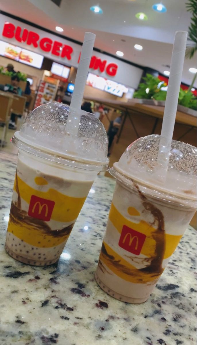 two plastic cups filled with ice cream and toppings on top of a marble counter