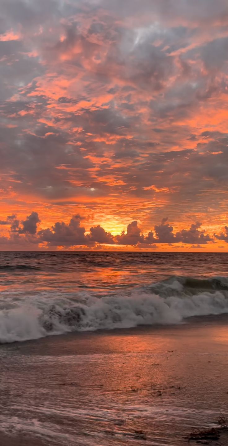 the sun is setting over the ocean with clouds in the sky and waves on the beach